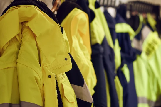 Rang&eacute;e de vestes de travail haute visibilit&eacute; jaunes suspendues sur cintres, avec v&ecirc;tements bleu marine en arri&egrave;re-plan