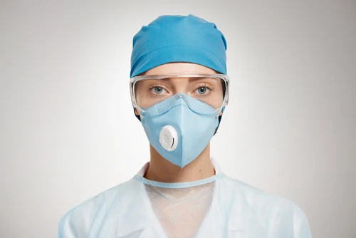 Personnel médical en tenue chirurgicale complète : charlotte bleue, masque respiratoire filtrant avec valve expiratoire, lunettes de protection transparentes et blouse stérile