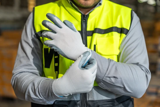 Paire de gants de travail en tricot gris pos&eacute;s sur fond blanc, avec liser&eacute; orange au niveau des poignets