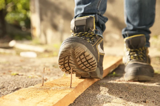 Personne assise sur des marches en b&eacute;ton, attachant une chaussure de s&eacute;curit&eacute; noire avec lacets orange