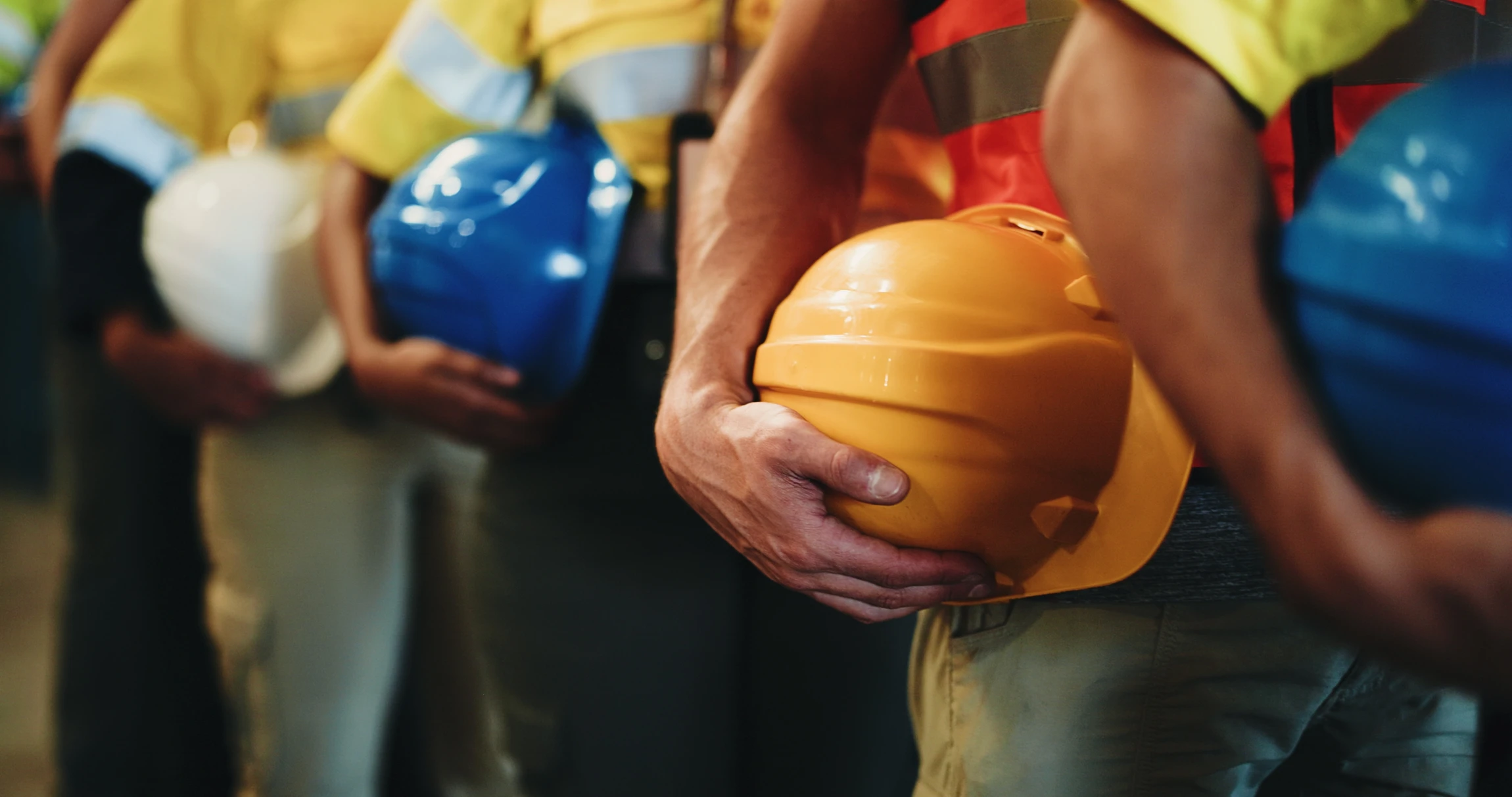 Ouvrier du bâtiment tenant un casque de sécurité jaune, portant une ceinture à outils garnie d'équipements de construction